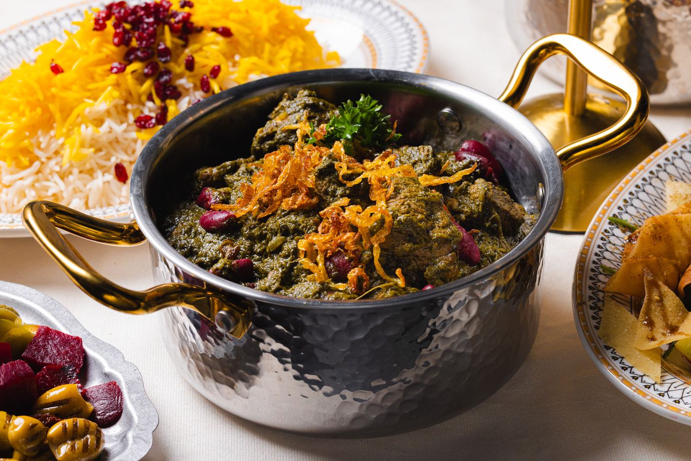 Ghormeh sabzi in a hammered copper pot beside saffron rice with barberries